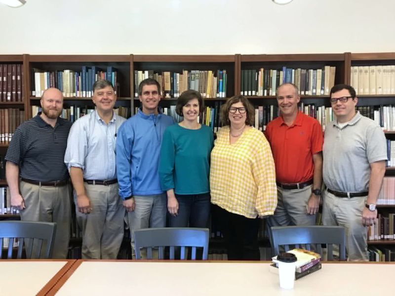 Seven members of the Currie Seminar standing together in front of library shelves